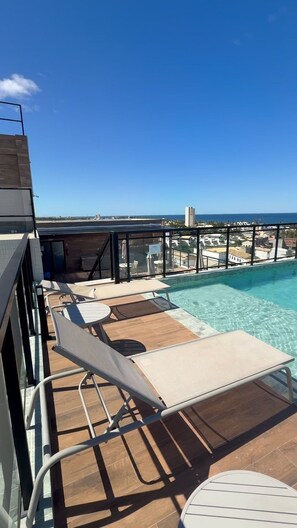 A rooftop pool area with lounge chairs and a view of the ocean.