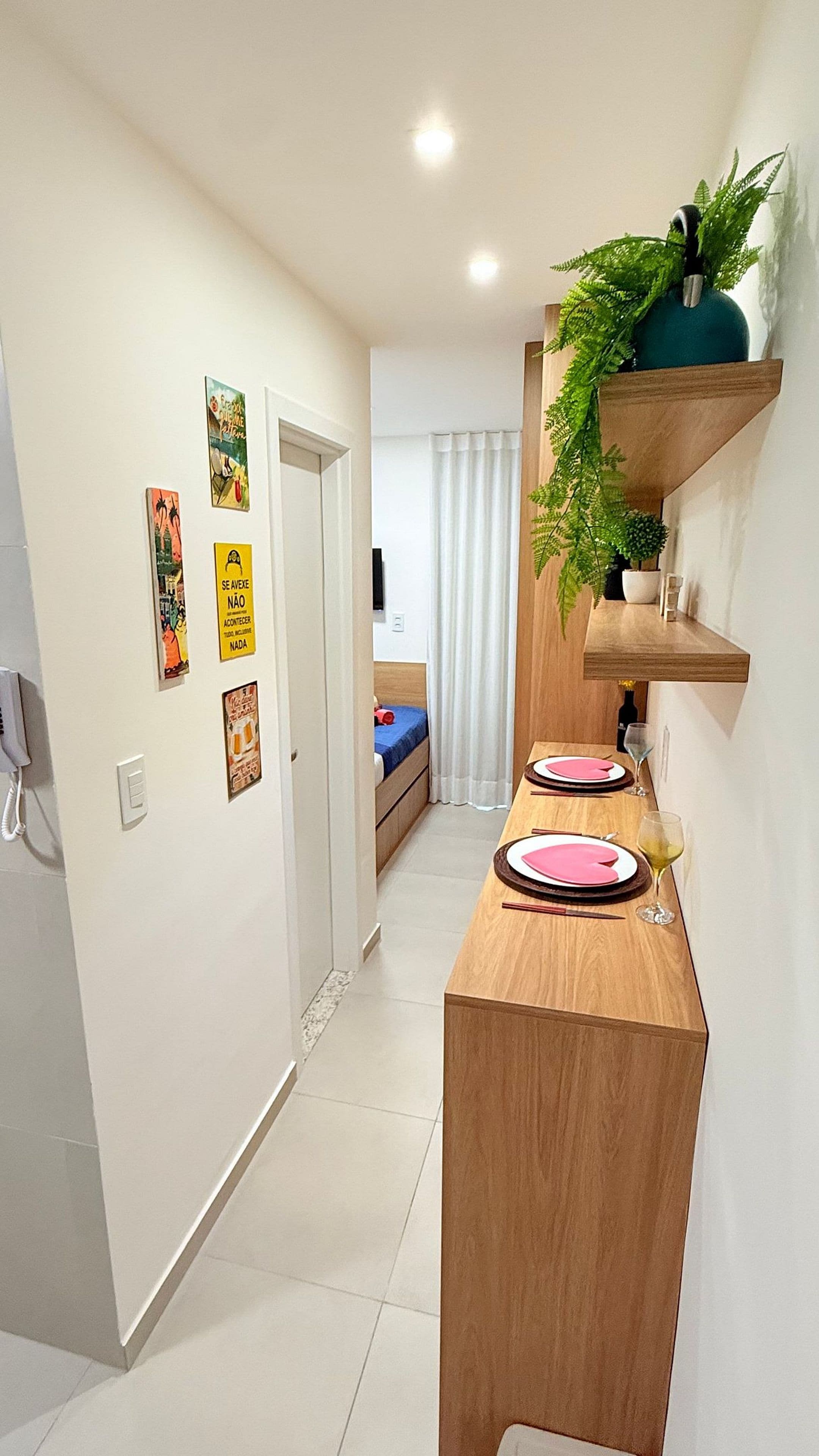Un pasillo con una mesa de madera preparada para comer, una cama con una colcha azul y una planta en un estante.
