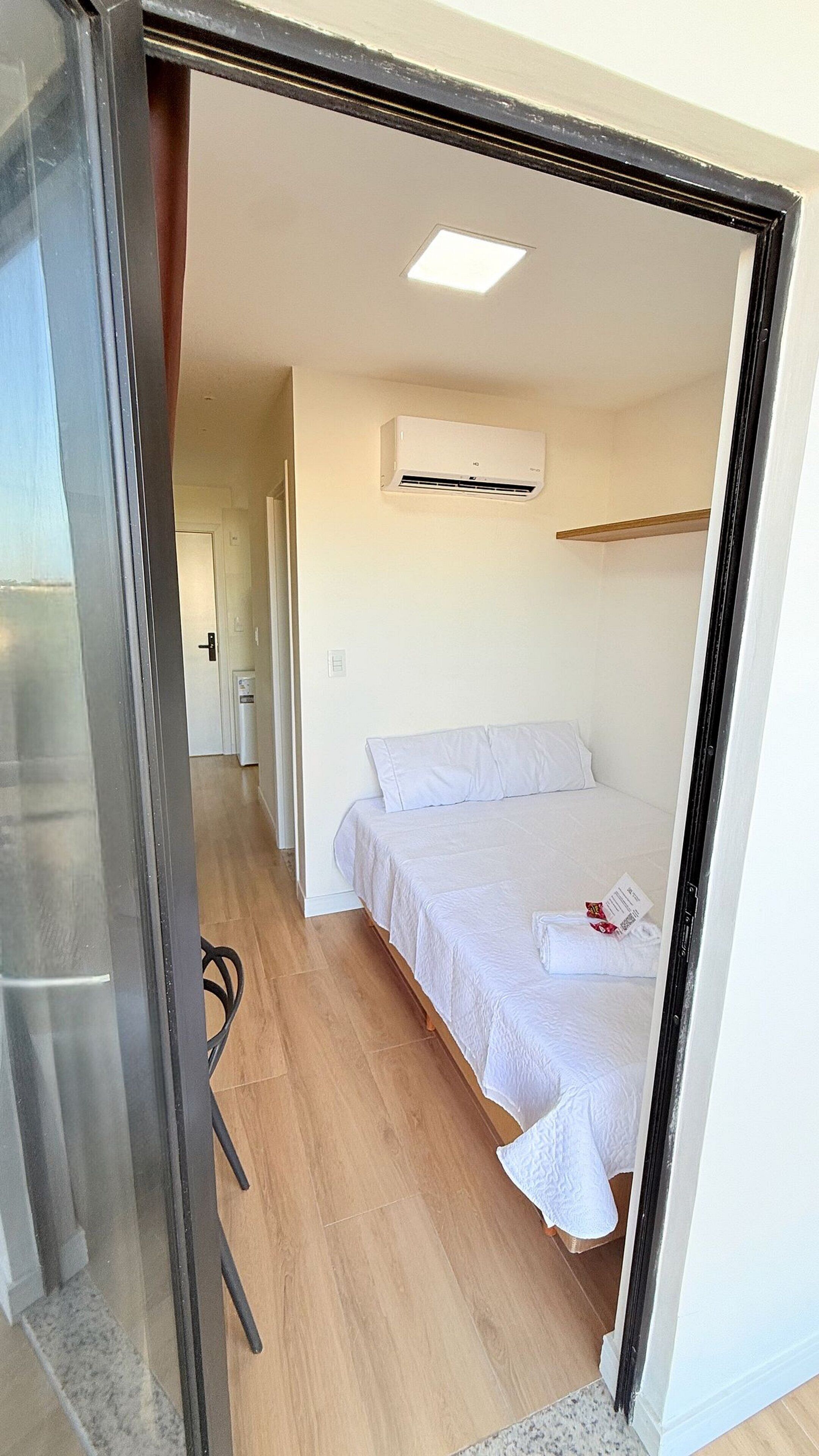 A bedroom with a bed, an air conditioning unit, and a door leading to another room.