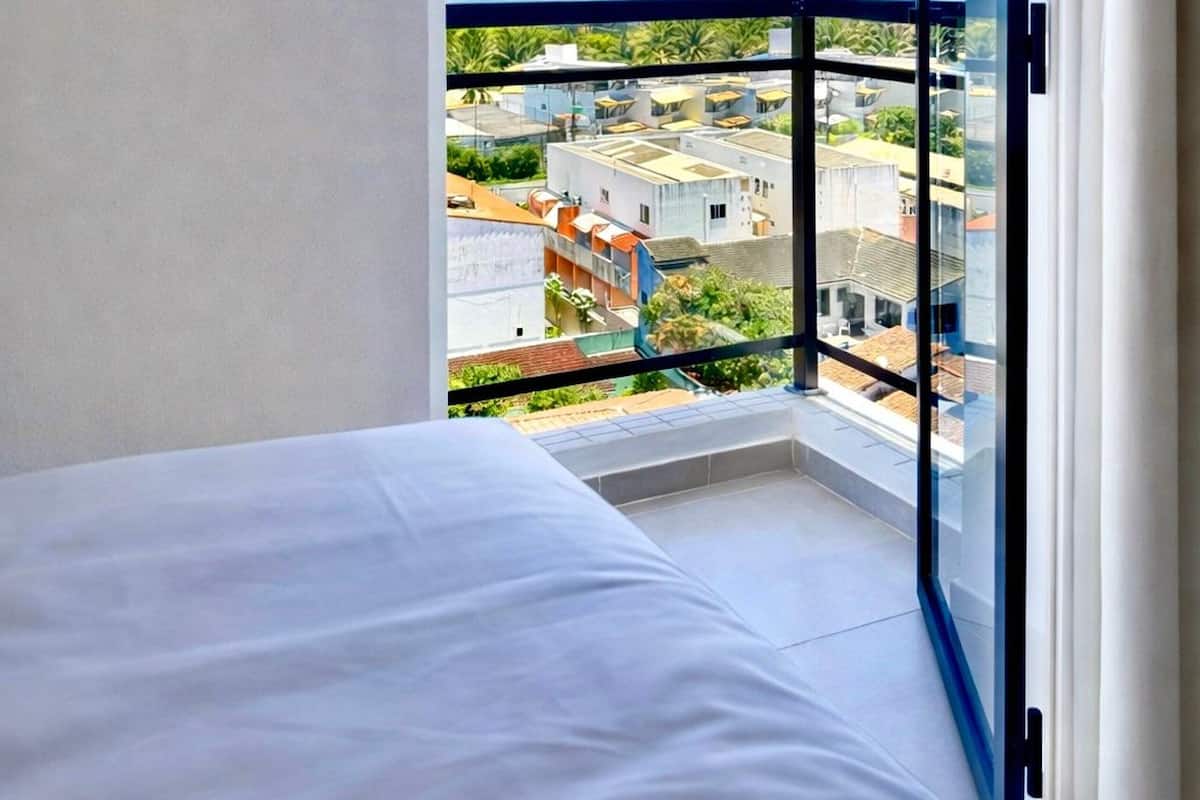 A bedroom with a large window, a bed, and a view of a cityscape.