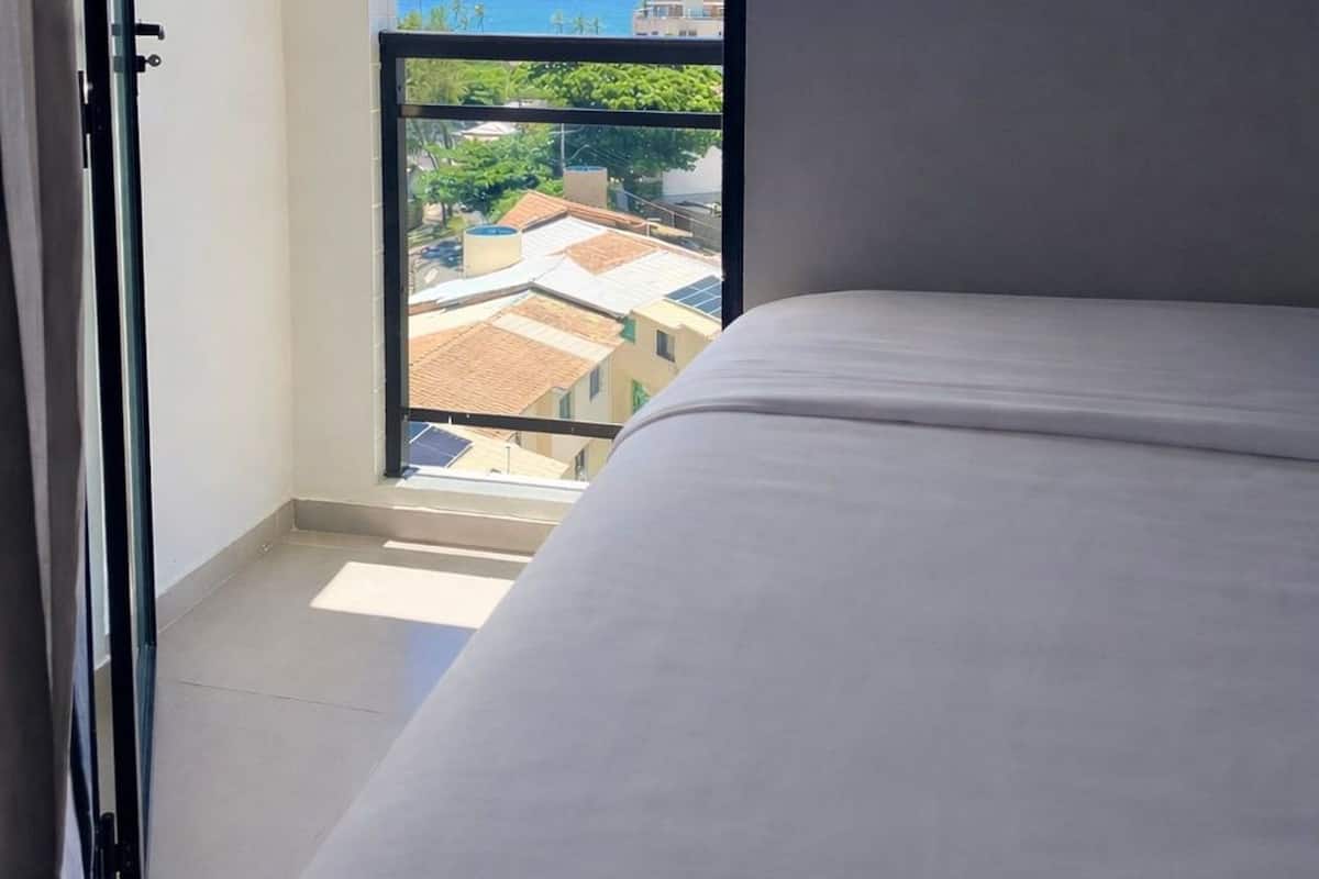 A balcony with a view of buildings and the sea, a bed, and a door.
