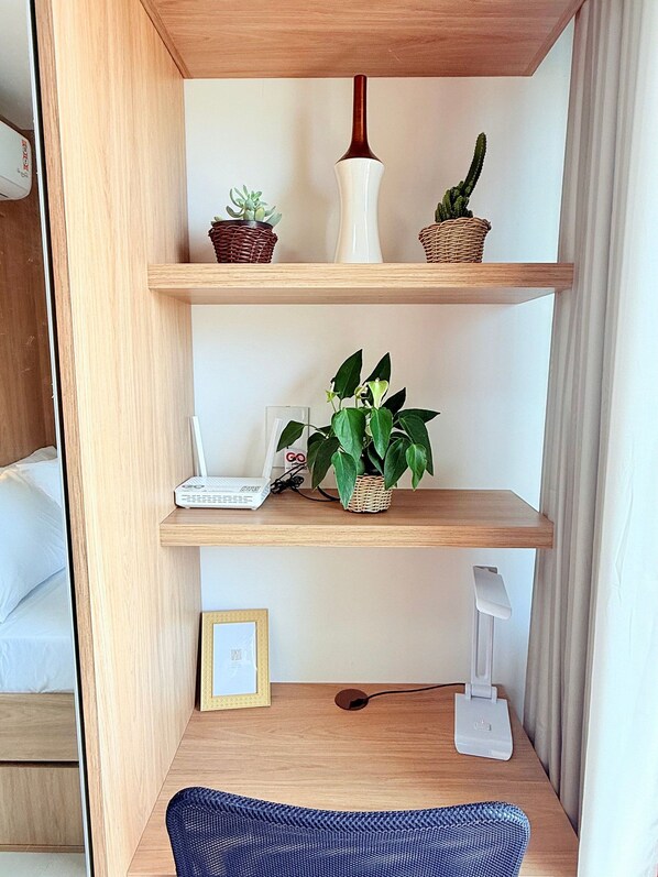 A wooden desk with a laptop, a plant, a white vase, and a cactus.