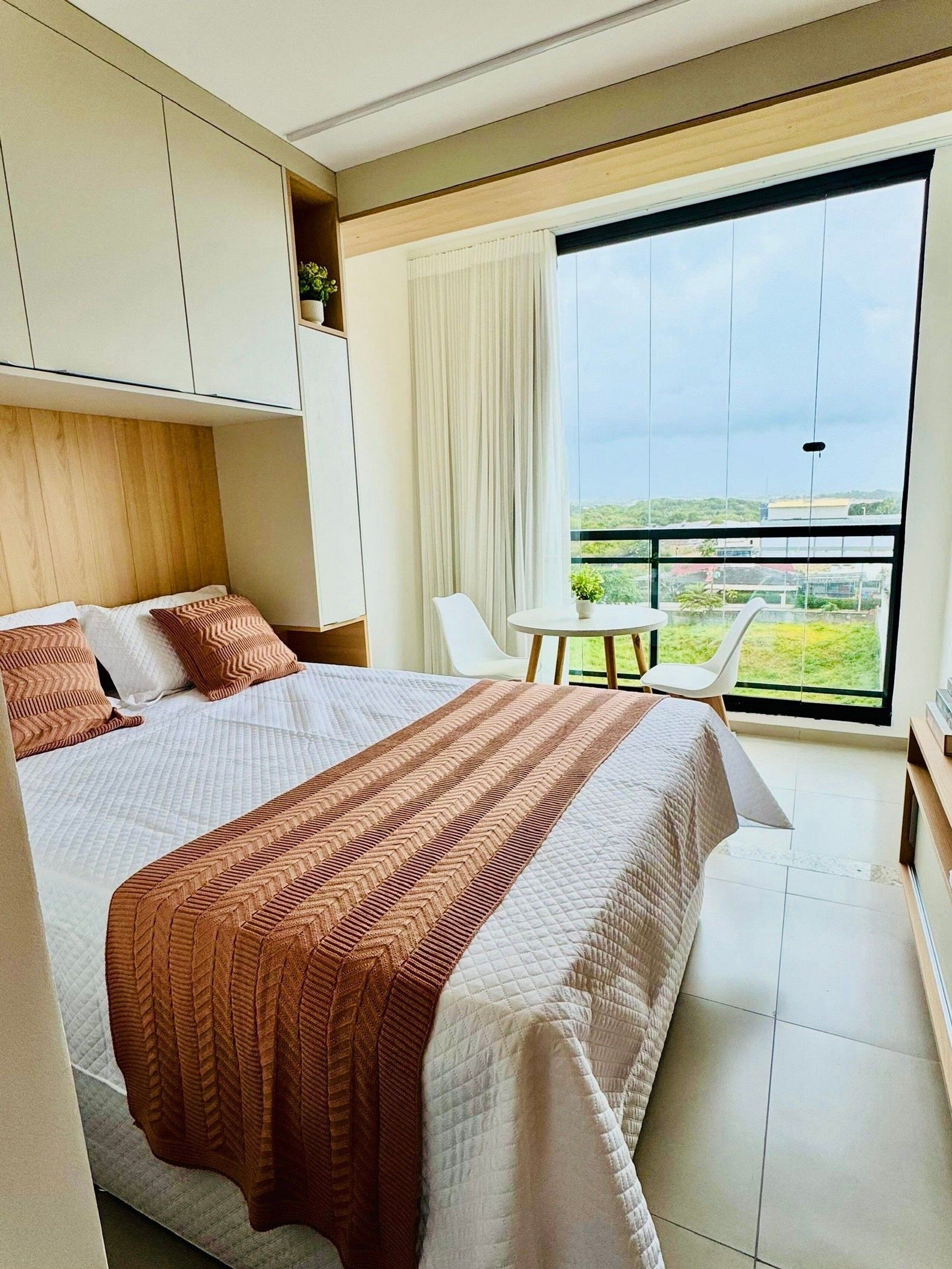 A modern bedroom with a large bed, a small table, and a balcony with a view.