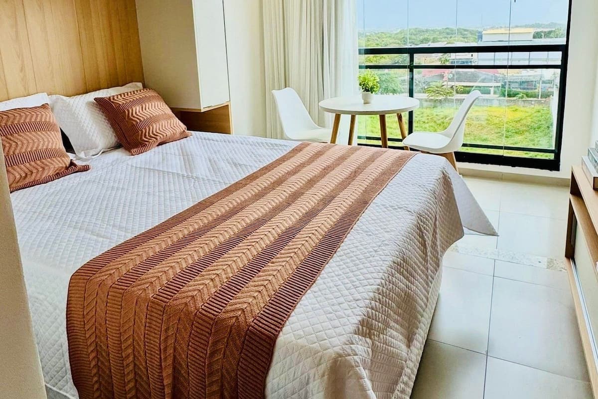 A modern bedroom with a large bed, a small table, and a balcony with a view.