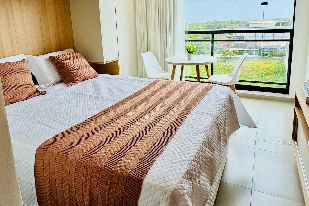 A modern bedroom with a large bed, a small table, and a balcony with a view.