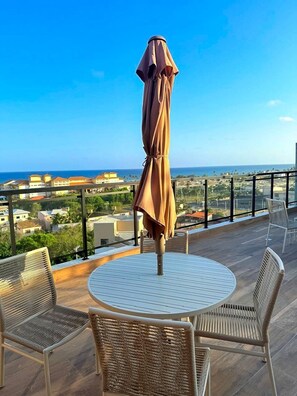 A balcony with a round table and wicker chairs, overlooking a coastal view. - Concept Life Stella (Salvador)