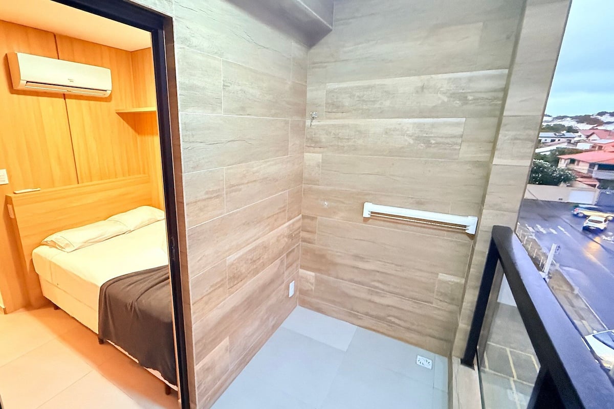 A small, modern room with a bed, a wooden wardrobe, and a shower area.