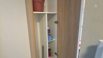 Une armoire entrouverte, avec des étagères contenant des produits de nettoyage et un seau rouge.