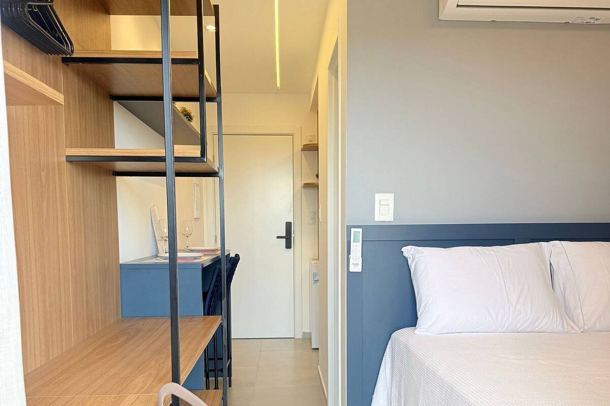 A hotel room with a bed, a desk, a chair, a wardrobe, and an air conditioning unit.