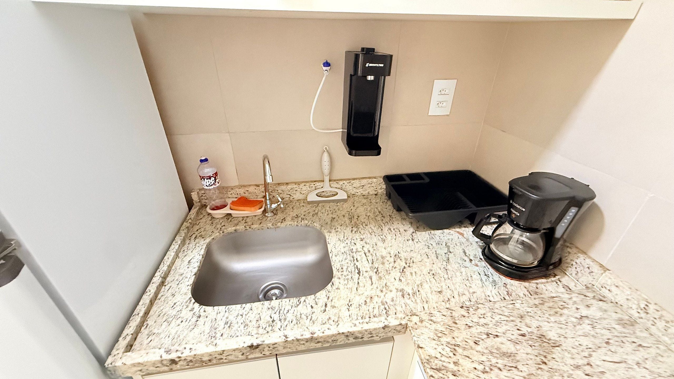 A kitchen with a sink, a coffee maker, a water dispenser, and a trash bin.