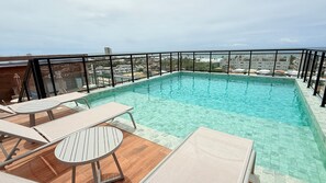 A rooftop pool with clear water, surrounded by a black metal railing and furnished with lounge chairs and tables. - Concept Life Stella (Salvador)