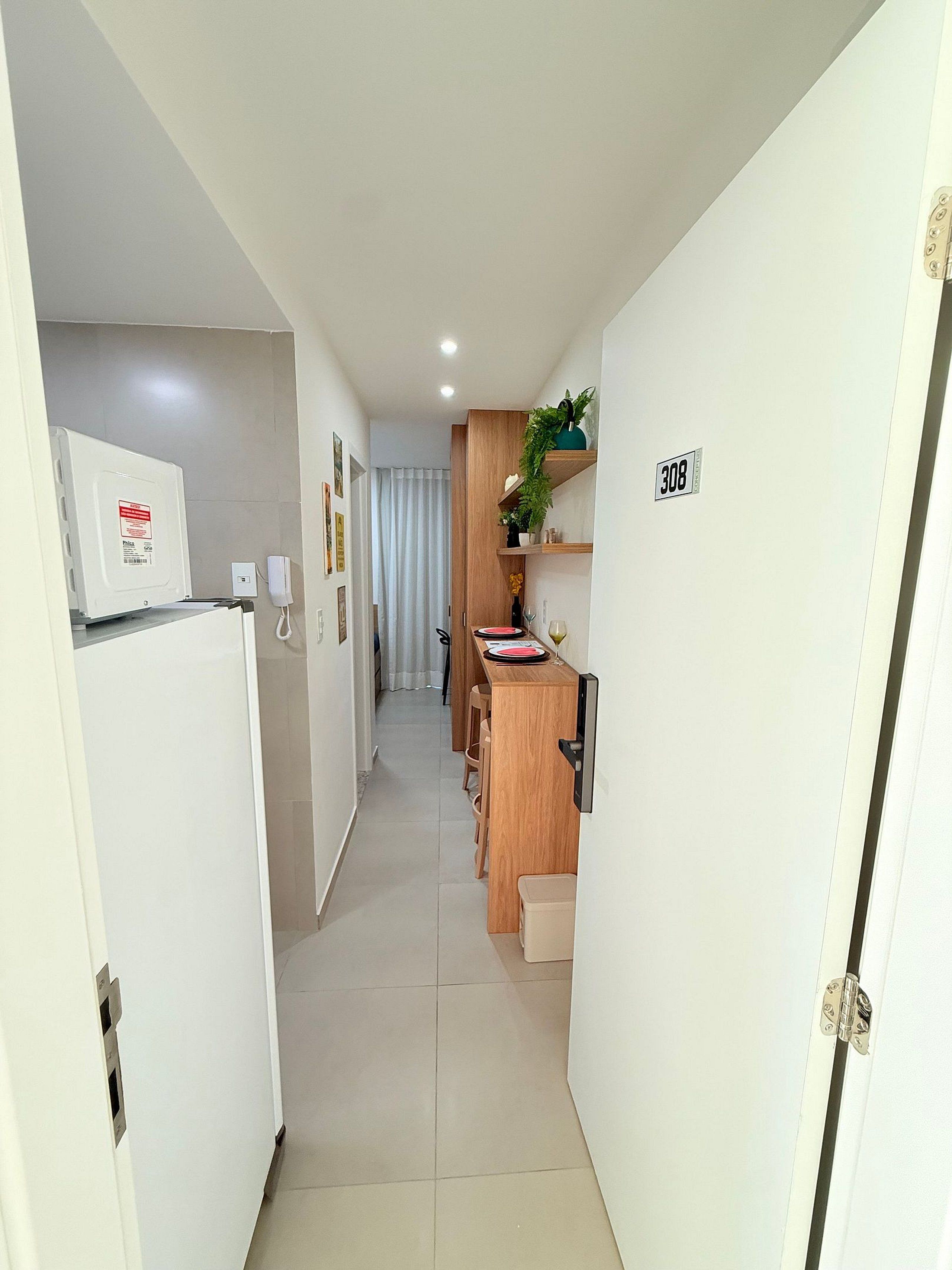 Corredor estreito com cozinha equipada, incluindo micro-ondas, pia e bancada de madeira.