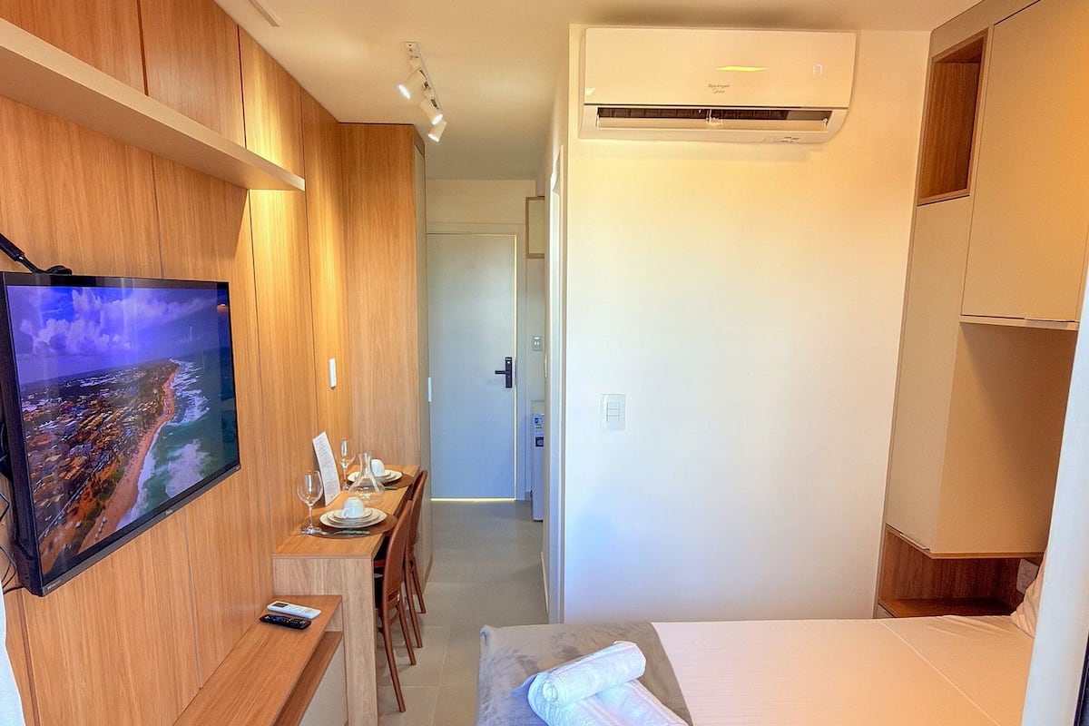 Una habitación de hotel con televisión, un escritorio con silla, cama y aire acondicionado.