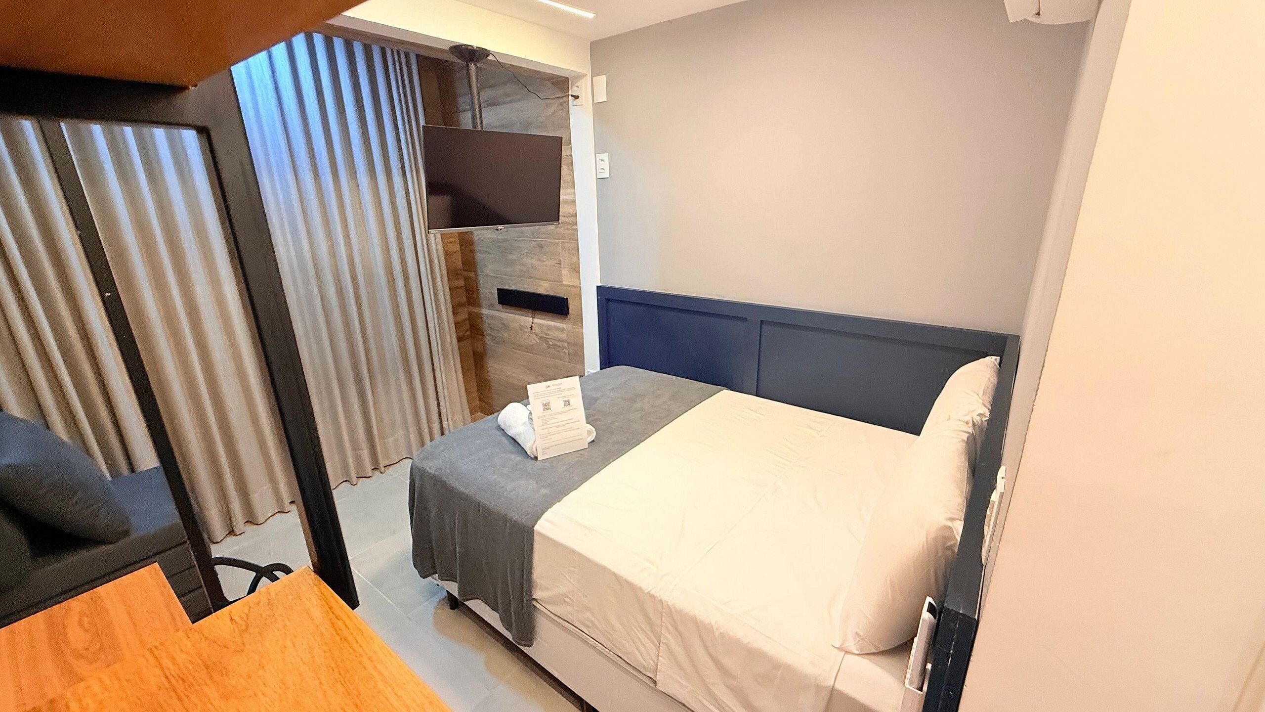 A hotel room with a bed, a desk, a chair, a TV, and a curtain.