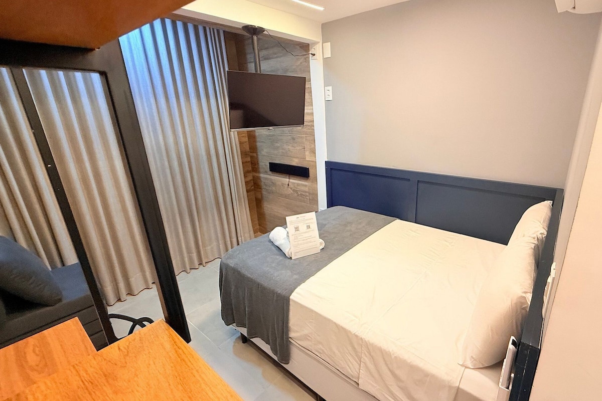A hotel room with a bed, a desk, a chair, a TV, and a curtain.