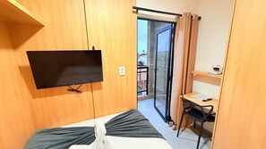 A room with a bed, a TV mounted on the wall, a desk with a chair, and a sliding glass door leading to an outdoor area.
