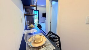 Un pasillo estrecho con una mesa de comedor dispuesta para dos personas, una cama y un televisor al fondo.