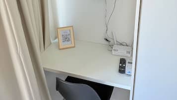 Un escritorio blanco con una silla negra, un cuadro enmarcado y un router en la pared.