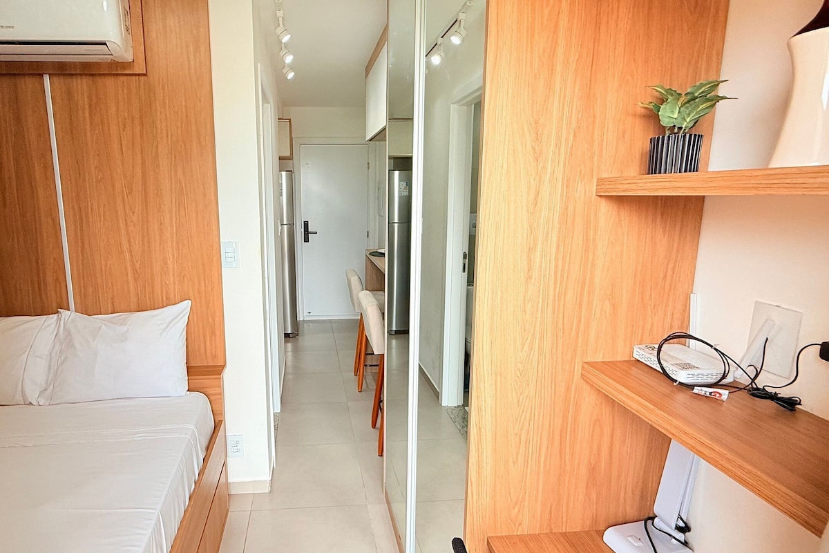 A bedroom with a bed, a desk with a computer, a mirror, and a small plant.