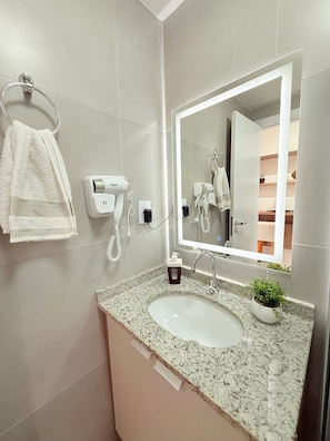 A bathroom with a sink, a mirror, a hairdryer, and a towel rack. - Concept Life Stella (Salvador)