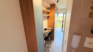 Un pasillo estrecho que conduce a un comedor con una mesa y sillas de madera, un estante con fotos enmarcadas y vistas a zonas verdes al exterior.