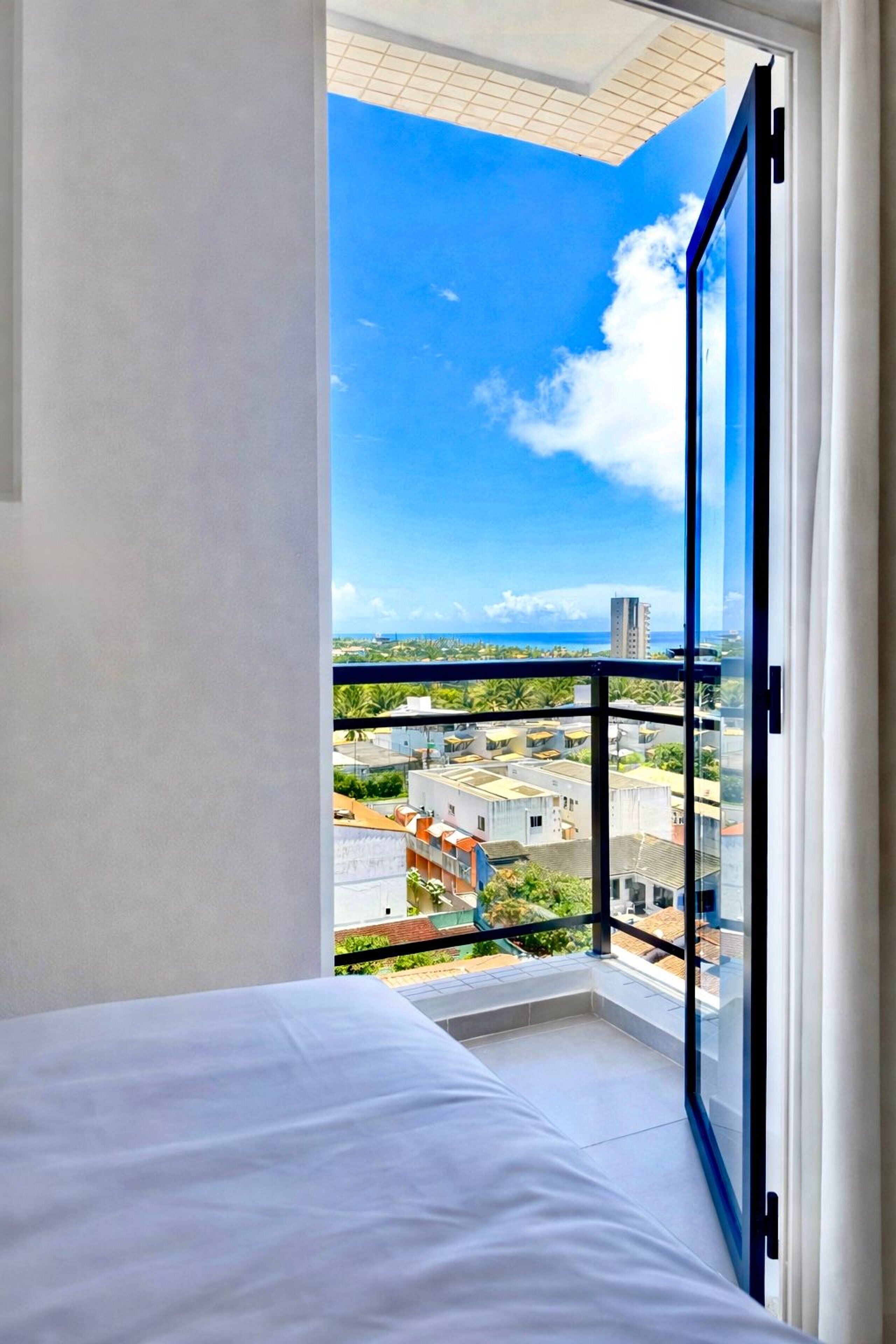 A bedroom with a large window, a bed, and a view of a cityscape.