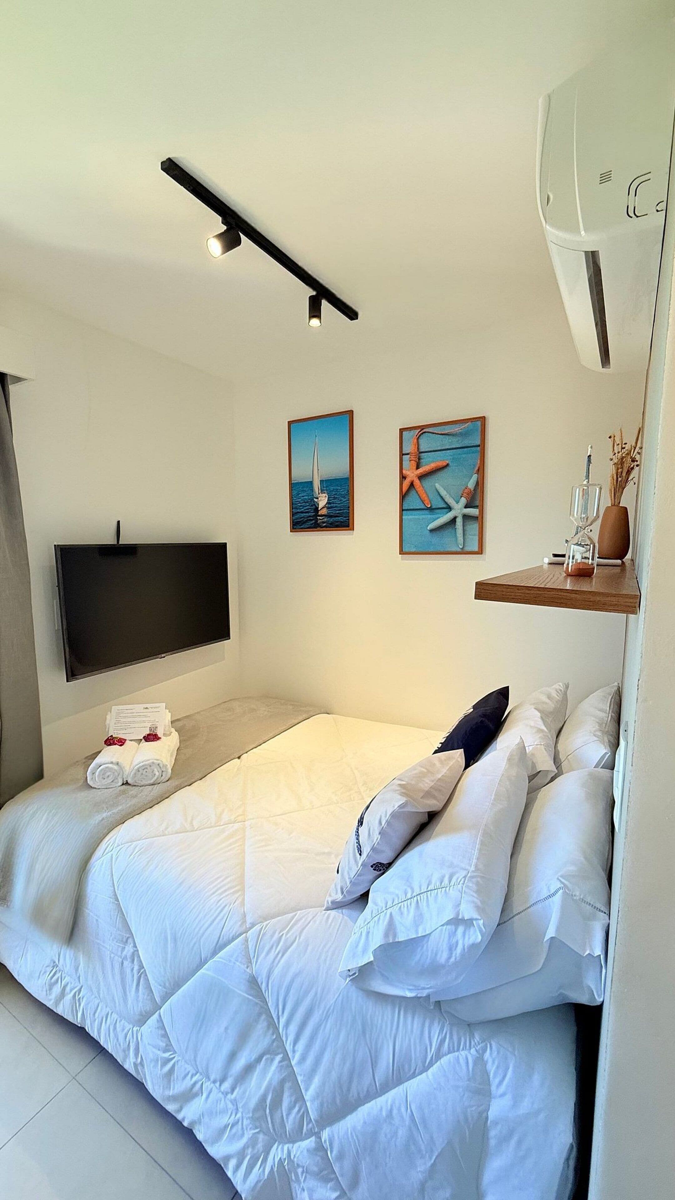 A modern bedroom with a bed, a flat-screen TV, artwork, and a built-in air conditioning unit.