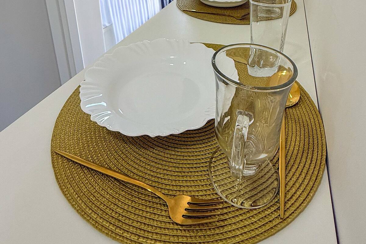 Un comedor con una mesa dispuesta para dos personas, un televisor montado en la pared y una ventana con cortinas.