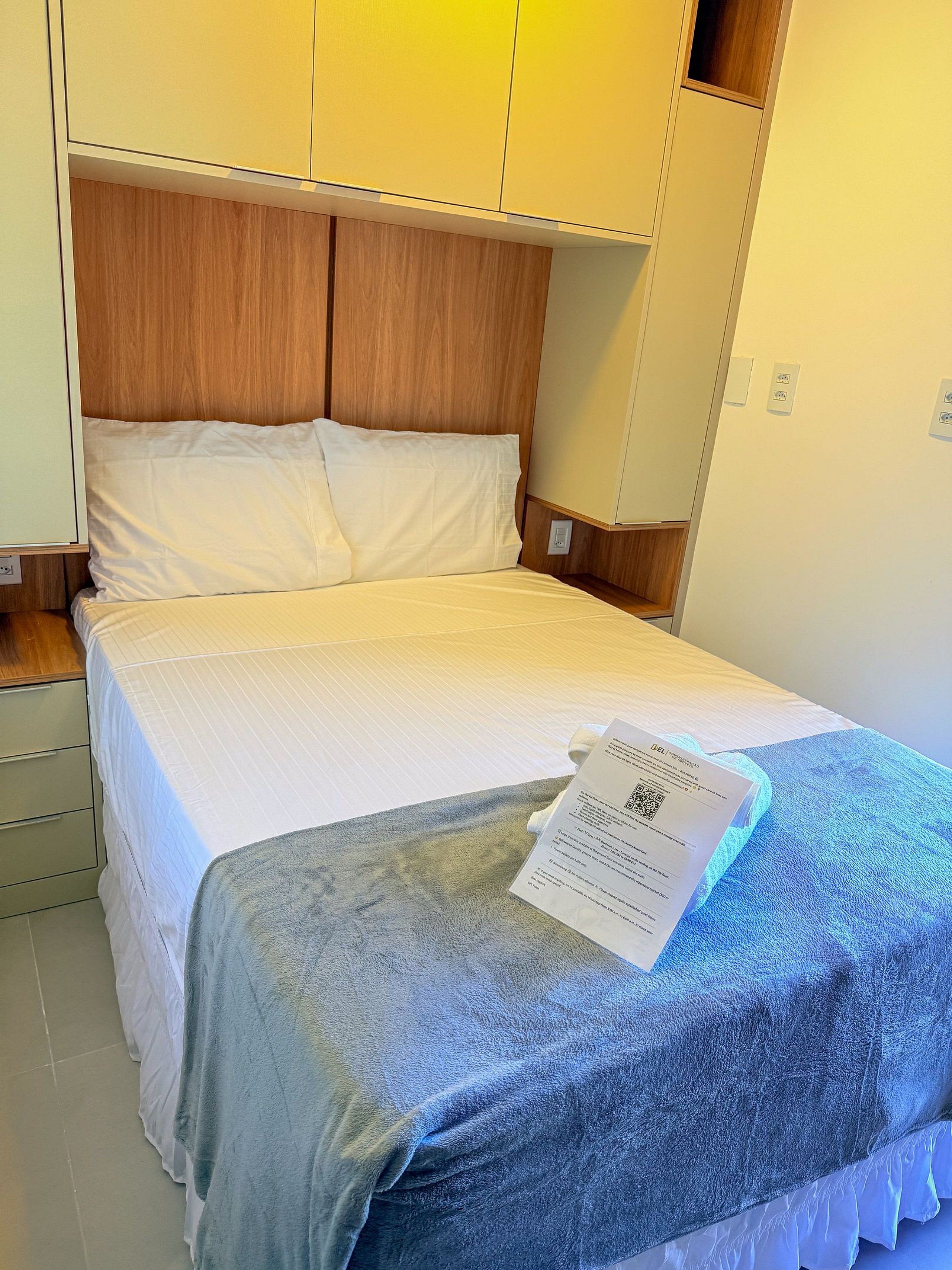 Hotellihuone, jossa on sänky, puinen pääty, valkoiset vuodevaatteet ja sininen pyyhe.
