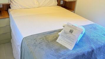 Une chambre d’hôtel avec un lit, une tête de lit en bois, du linge de lit blanc et une serviette bleue.
