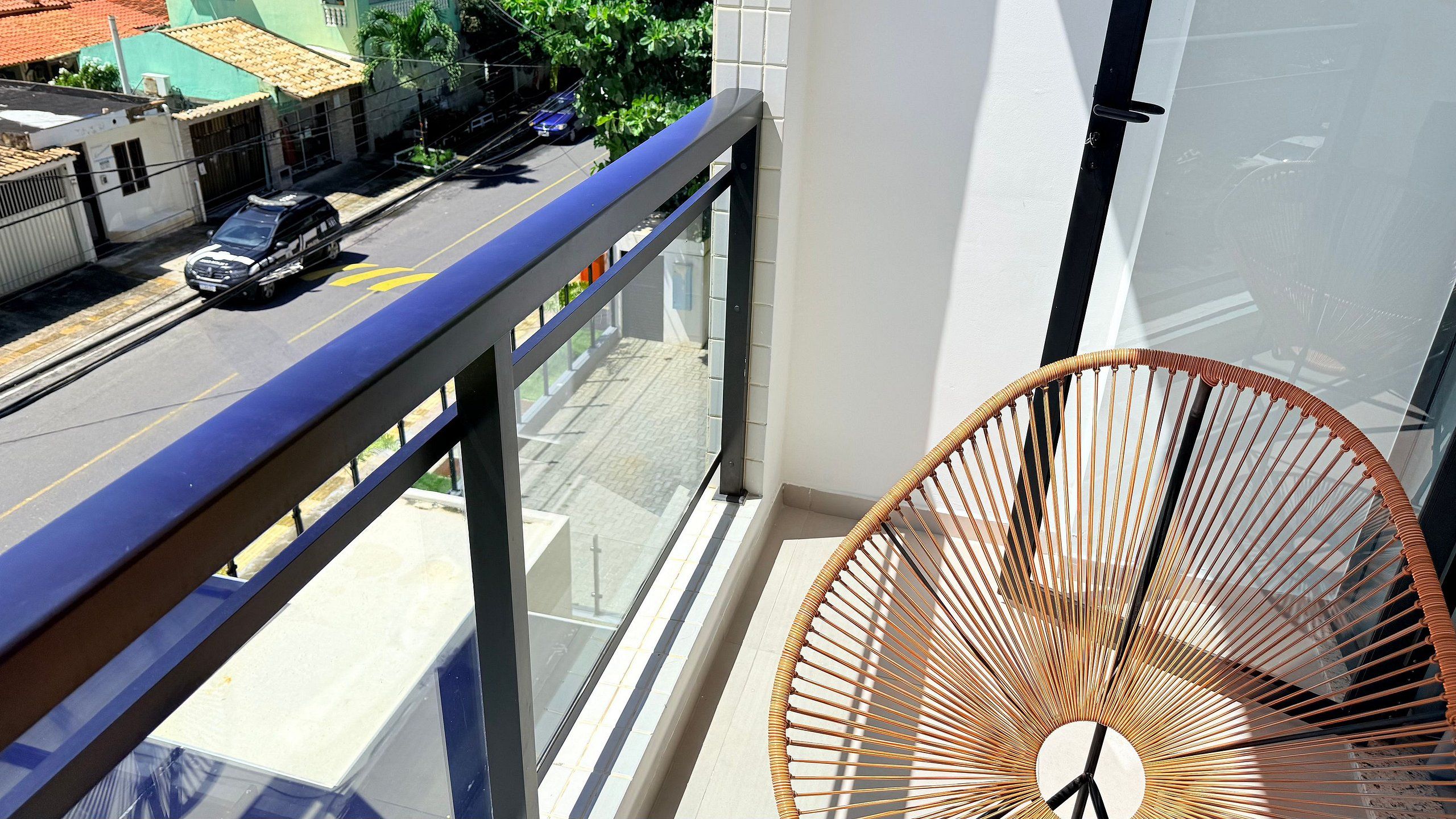 A balcony with a metal railing, a wicker chair, and a view of a street with cars and buildings.