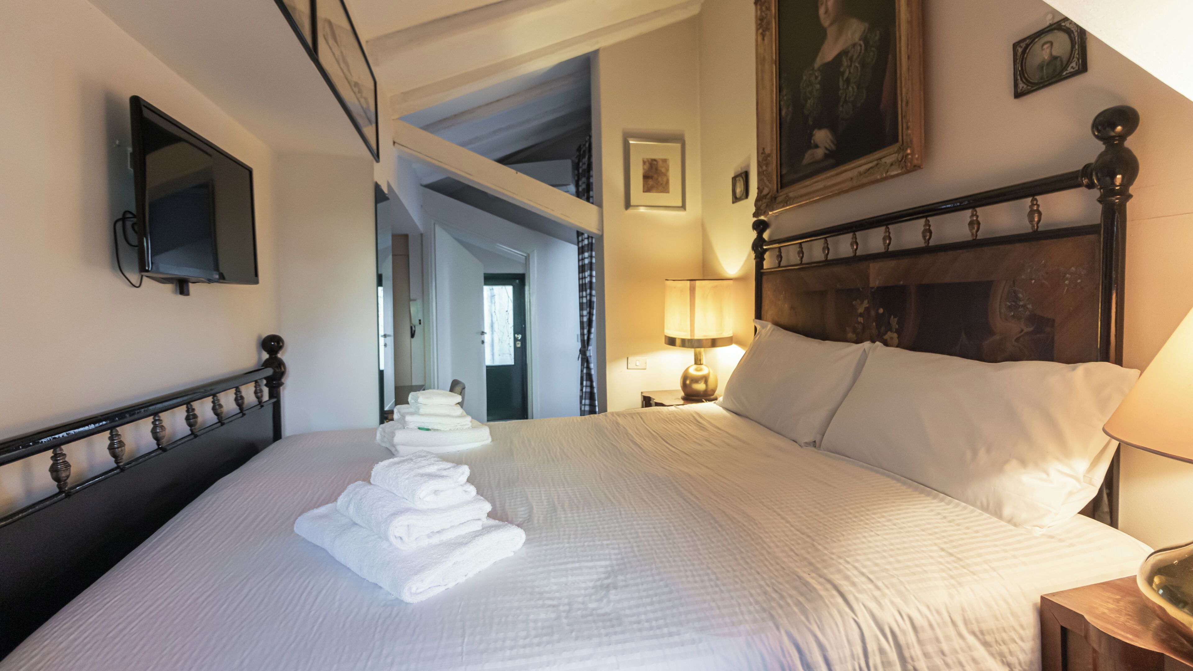 A hotel room with a neatly made bed, a bedside lamp, a painting on the wall, and a mirror on the wall.