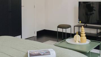 A modern bedroom with a green bedspread, a book on the bed, a TV on a stand, and a decorative wall piece.