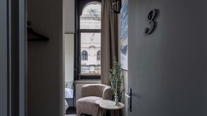 A narrow hallway with a chair and a small table, a number '3' on the wall, and a window with a view of a building. - Elegant Balcony Suite (Antwerpen)
