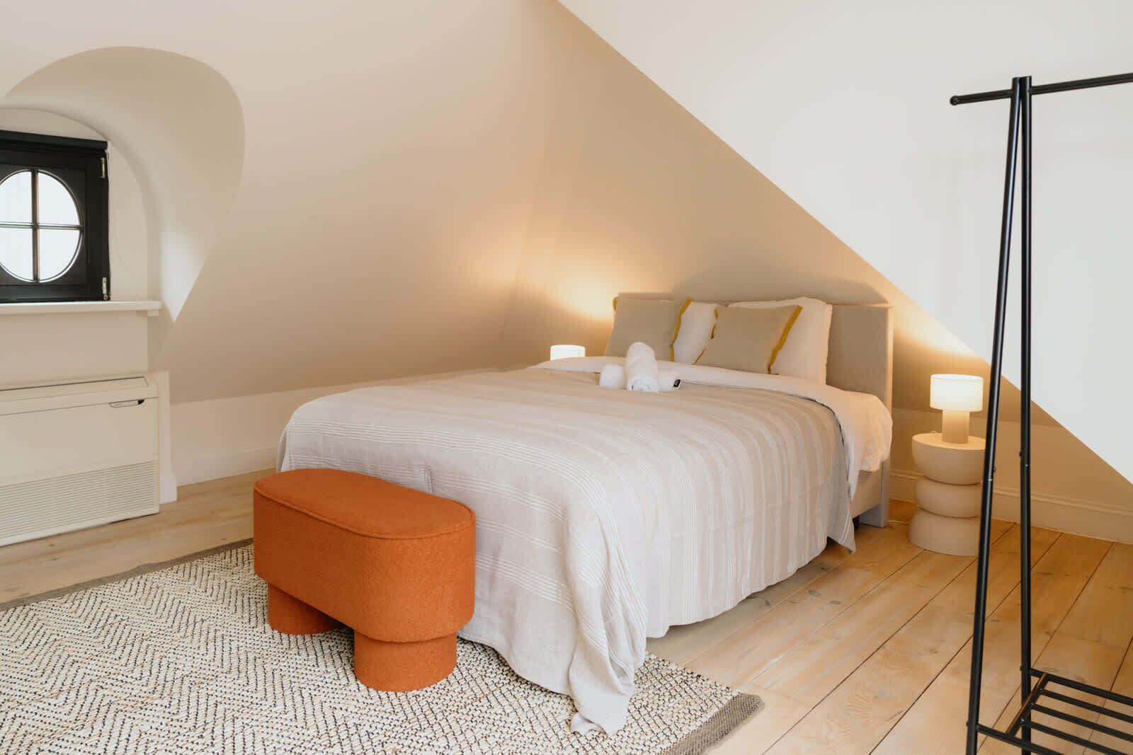 Ein Schlafzimmer mit Bett, Nachttisch, Lampe, Heizung und Fenster.