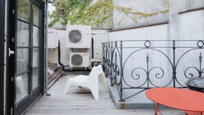 A wooden deck with a metal railing, a white plastic chair, a red metal table, and two air conditioning units labeled "SANYO". - Stylish Duplex Getaway in the Heart of Antwerp (Antwerpen)