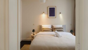 A neatly arranged hotel room with a large bed, two bedside lamps, a wall-mounted light, and a framed artwork above the bed. - Stylish Duplex Getaway in the Heart of Antwerp (Antwerpen)