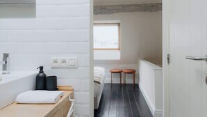 A modern bathroom with a white tiled wall, a wooden countertop, a black soap dispenser, and a white towel. - Spacious 3-Level Apartment in Mechelen (Mechelen)