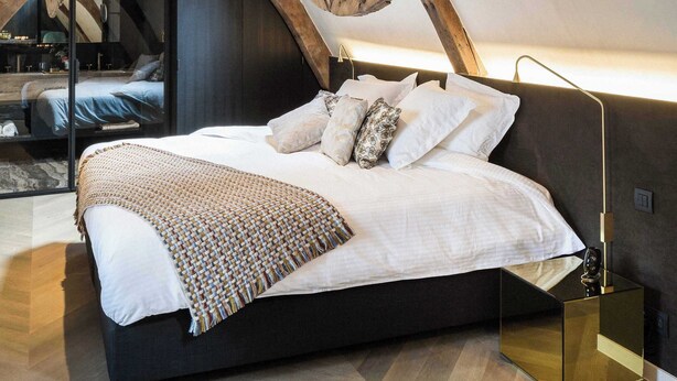 Une chambre avec un grand lit, des poutres en bois et une lucarne.
