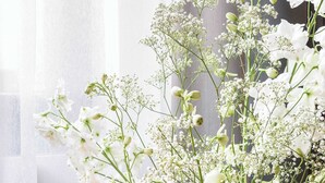 Une pièce comprenant un grand radiateur cylindrique de couleur sombre et un bouquet de fleurs blanches dans un vase.