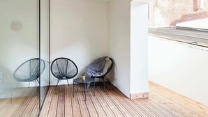 A small, open balcony with wooden flooring, two black wireframe chairs, a small round table with a potted plant, and a view of a brick building through a glass wall. - Magnificent 3BR home in Antwerp (Antwerpen)