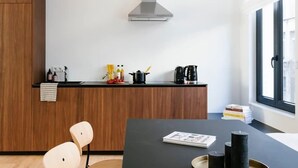 A modern kitchen with a black countertop, wooden chairs, and a central island with a tray. - Magnificent 3BR home in Antwerp (Antwerpen)
