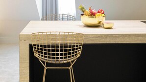 Moderni ruokailutila, jossa on betonisesta materiaalista valmistettu pöytä, metallinen tuoli ja hedelmäkulho.