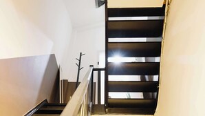 Eine enge Treppe mit Metallgeländer, die zu einer Zwischenebene mit einer Tür führt.
