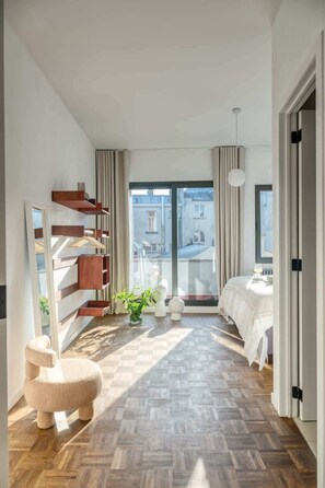 Une chambre moderne dotée d’une grande fenêtre, d’un plancher en bois, d’un lit, d’une chaise et d’une bibliothèque intégrée.