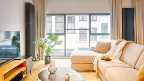 A modern living room with a large window, a sofa, a coffee table, and a TV.