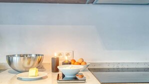 A kitchen counter with a large mixing bowl, a small bowl with butter, a scale, and a candle.