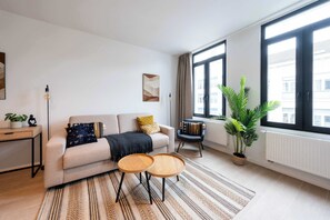 A modern living room with a sofa, two small tables, a potted plant, and large windows. - Modern 6-Guest Apartment in Central Antwerp (Antwerpen)