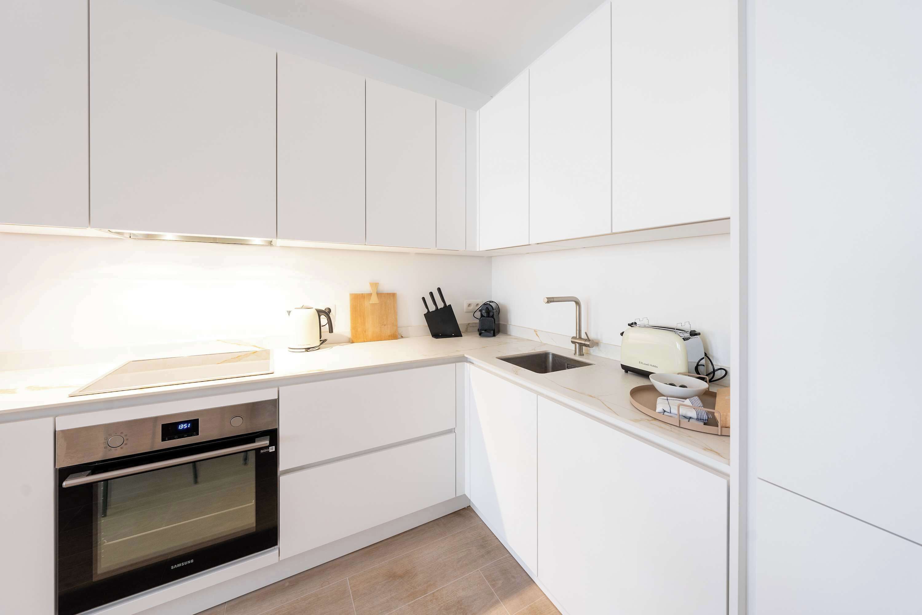 A modern kitchen with white cabinetry, a built-in oven, a sink, and a toaster.