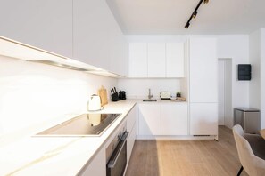 Eine moderne Küche mit weißen Schränken, einem Backofen, einem Herd und einer kleinen Essecke mit einem Stuhl.